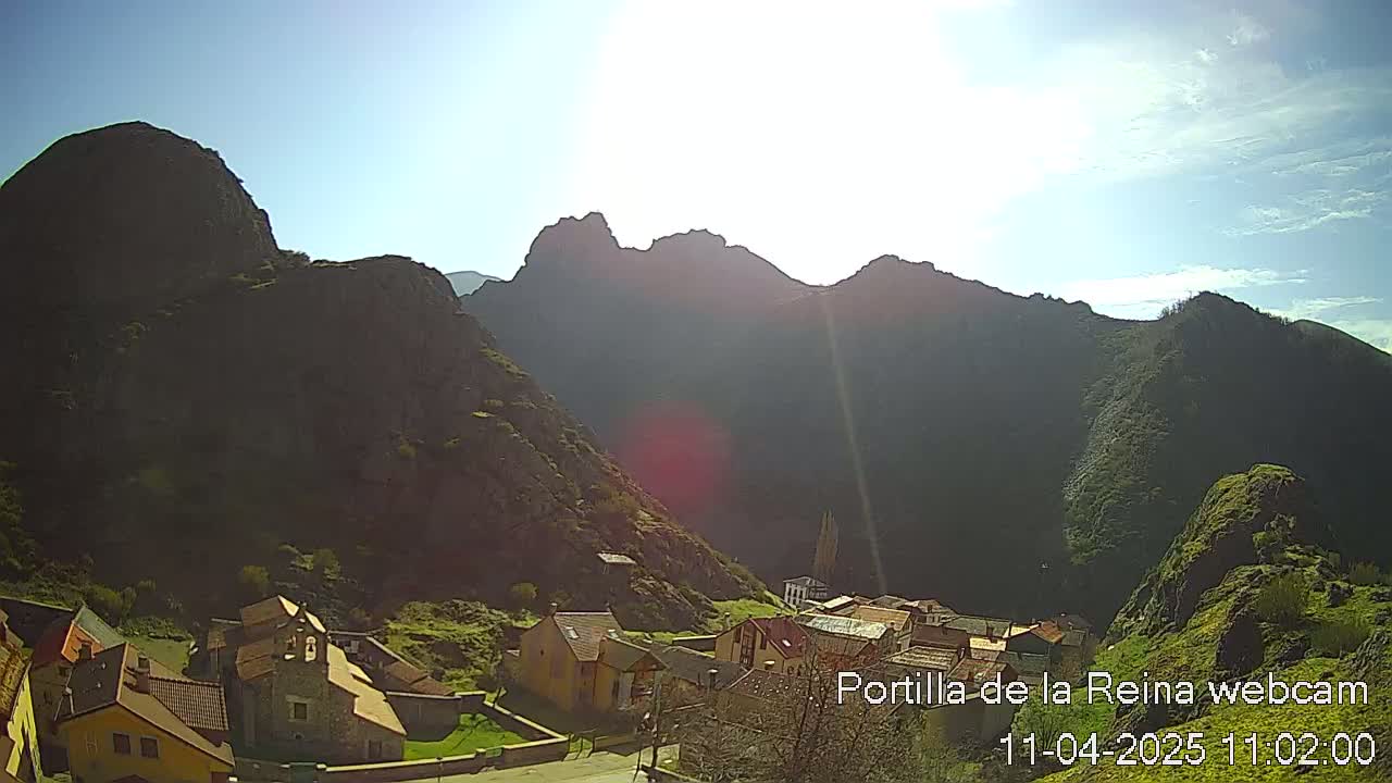 A sunny day reveals a small village nestled in a valley surrounded by dark, rocky mountains.
