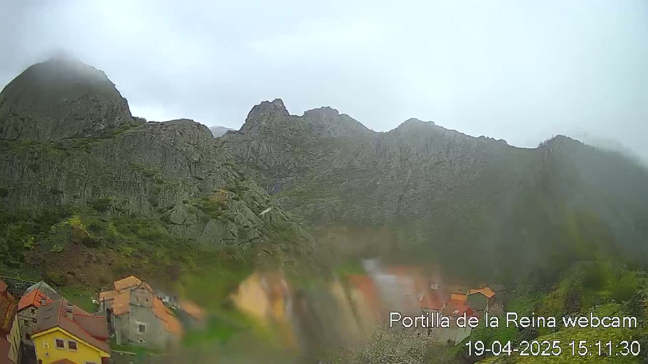 A foggy, overcast day reveals a rocky mountain range overlooking a small village nestled in the valley below.