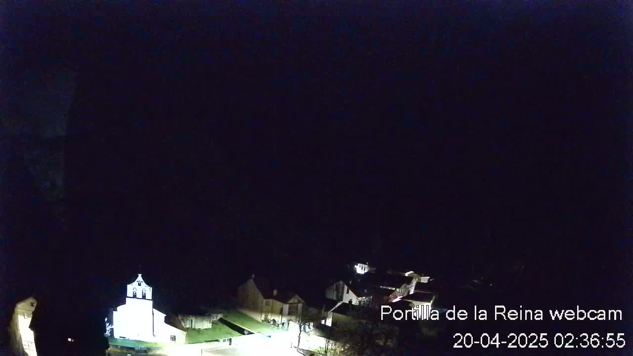 A nighttime, overhead view of a small village with a brightly lit church.