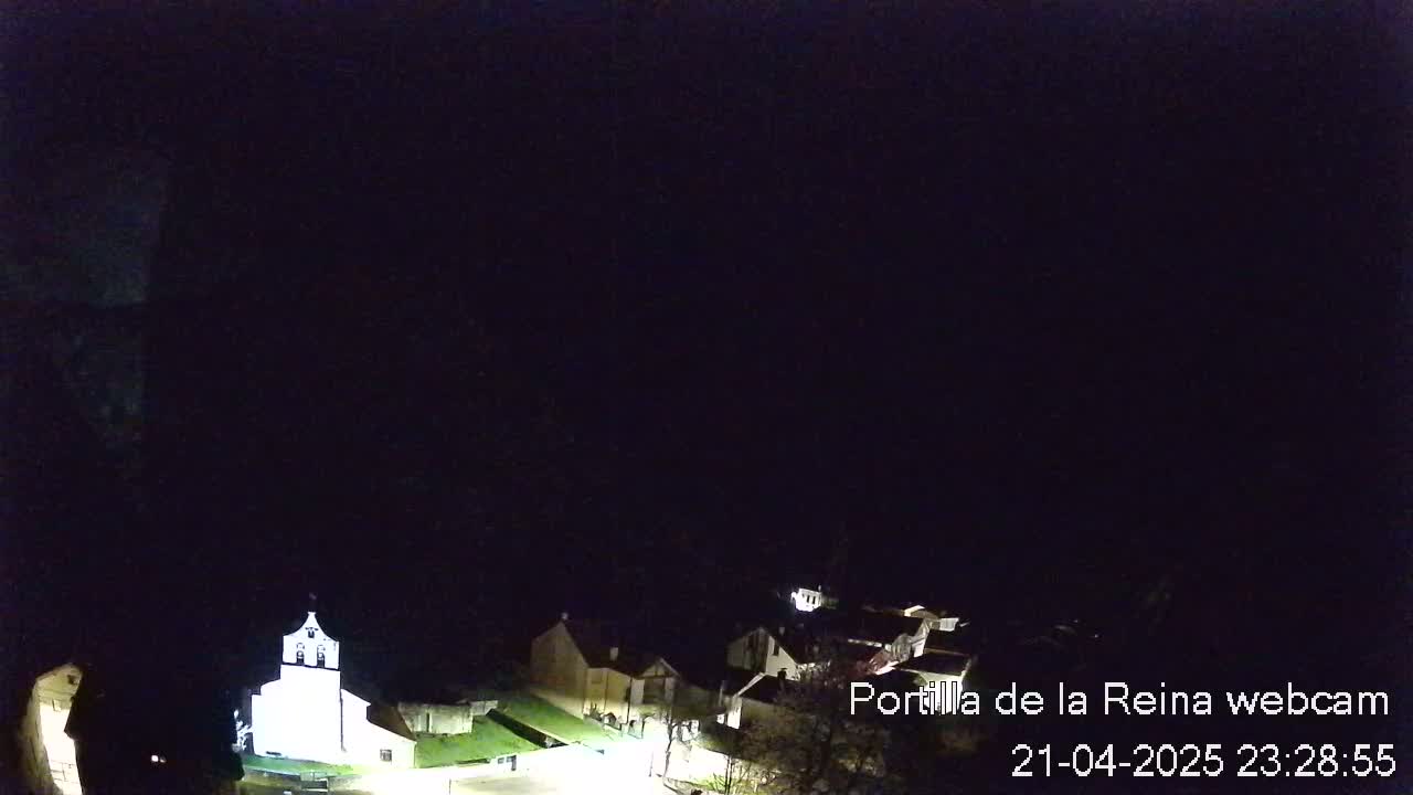 A nighttime, high-angle view shows a small village with a brightly lit church, under a dark, clear sky.