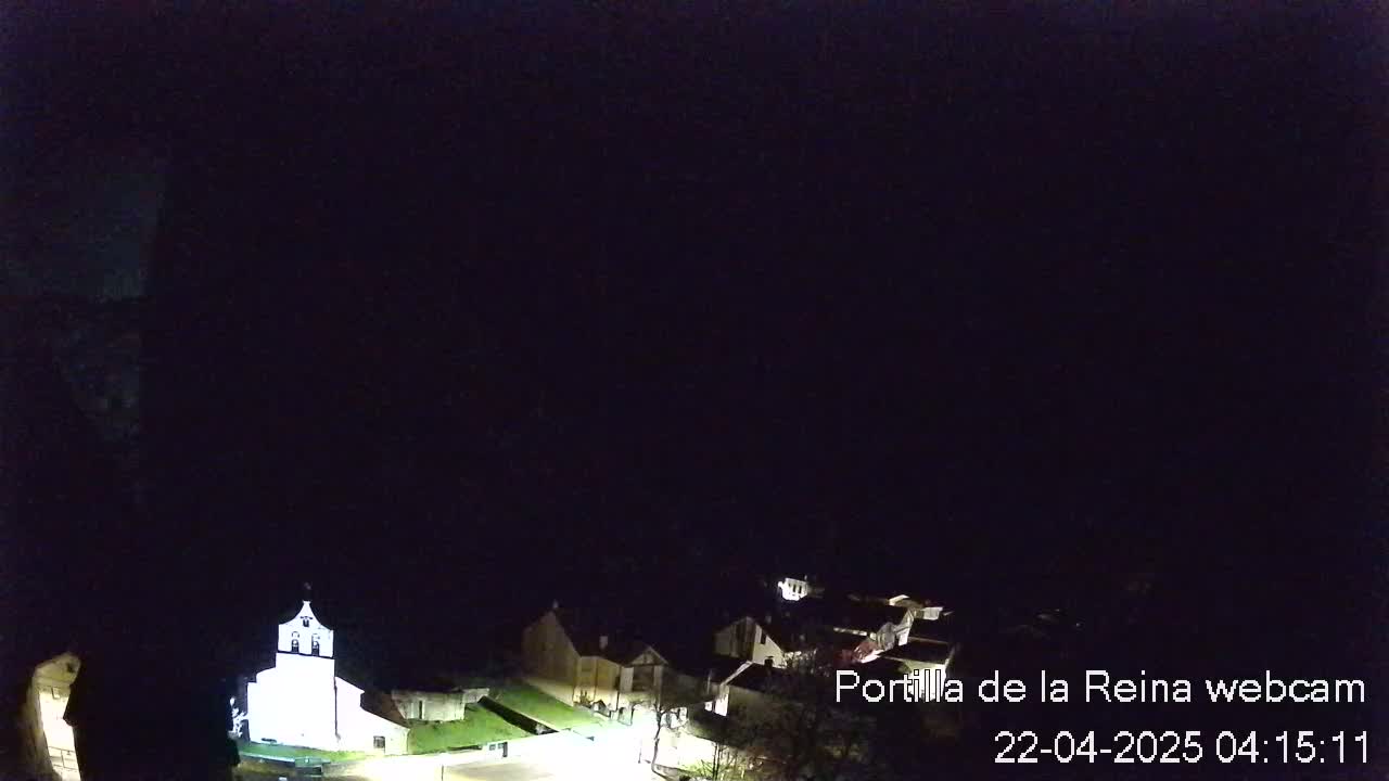 A nighttime, high-angle view of a small village with a brightly lit church, under a dark, clear sky.