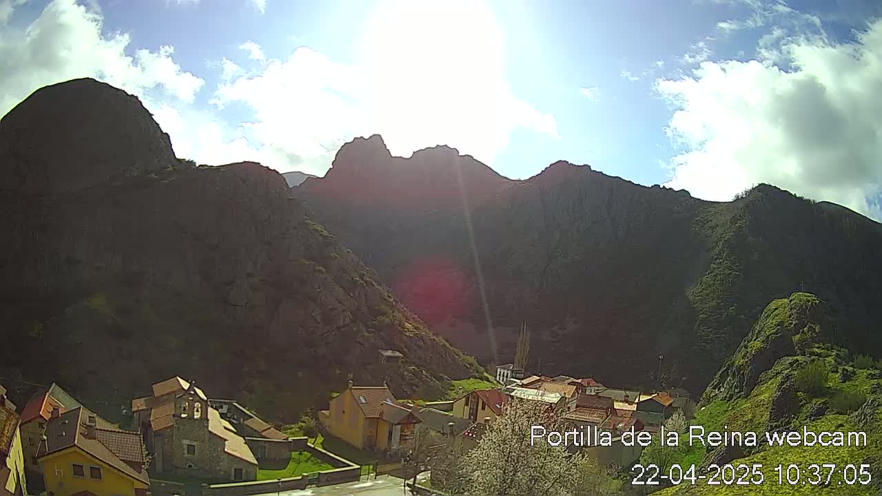 A sunny day reveals a village nestled in a valley between steep, dark-colored mountains.
