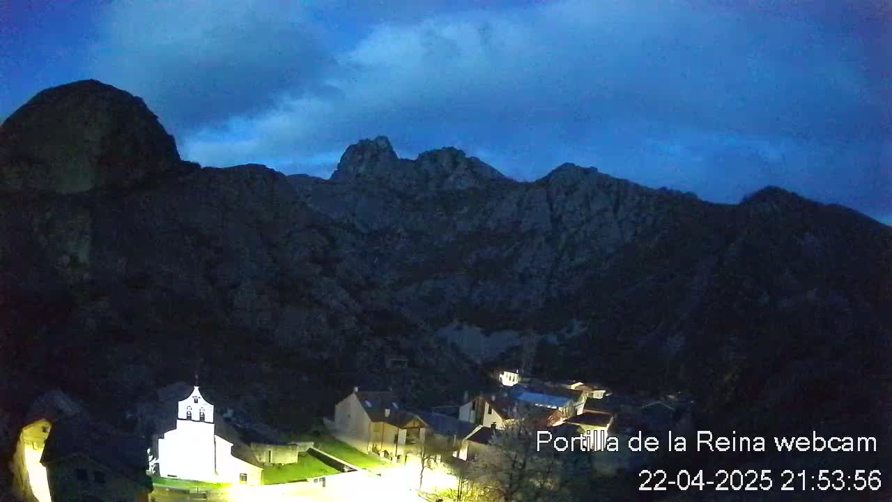 A small village nestled in a valley between dark, rocky mountains under a twilight sky.