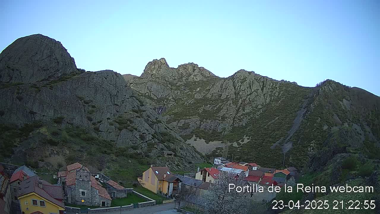 A small village nestled at the base of a large, rocky mountain under a clear blue sky.