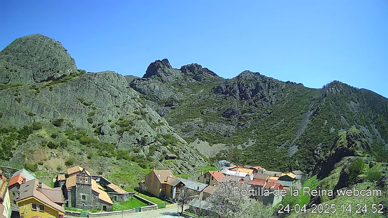 A small village nestled in a valley between rocky, green-covered mountains under a clear blue sky.