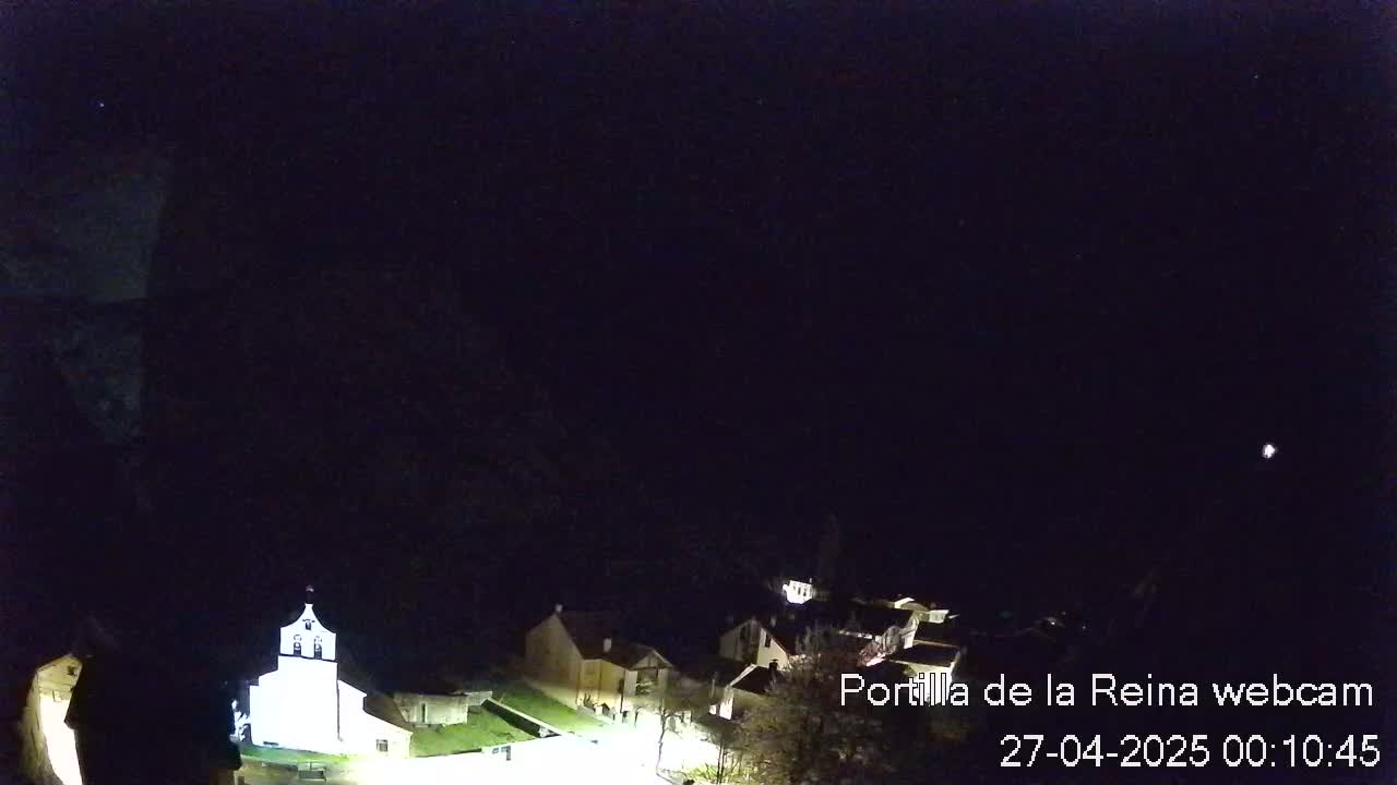 A nighttime view of a small village nestled against a dark mountainside under a clear, starlit sky.