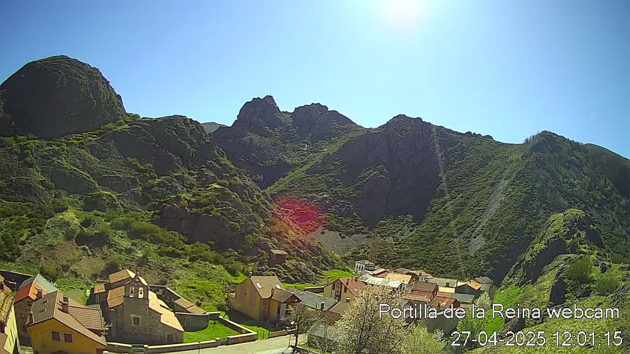 A small village nestled in a valley surrounded by large, rocky mountains under a bright, sunny sky.