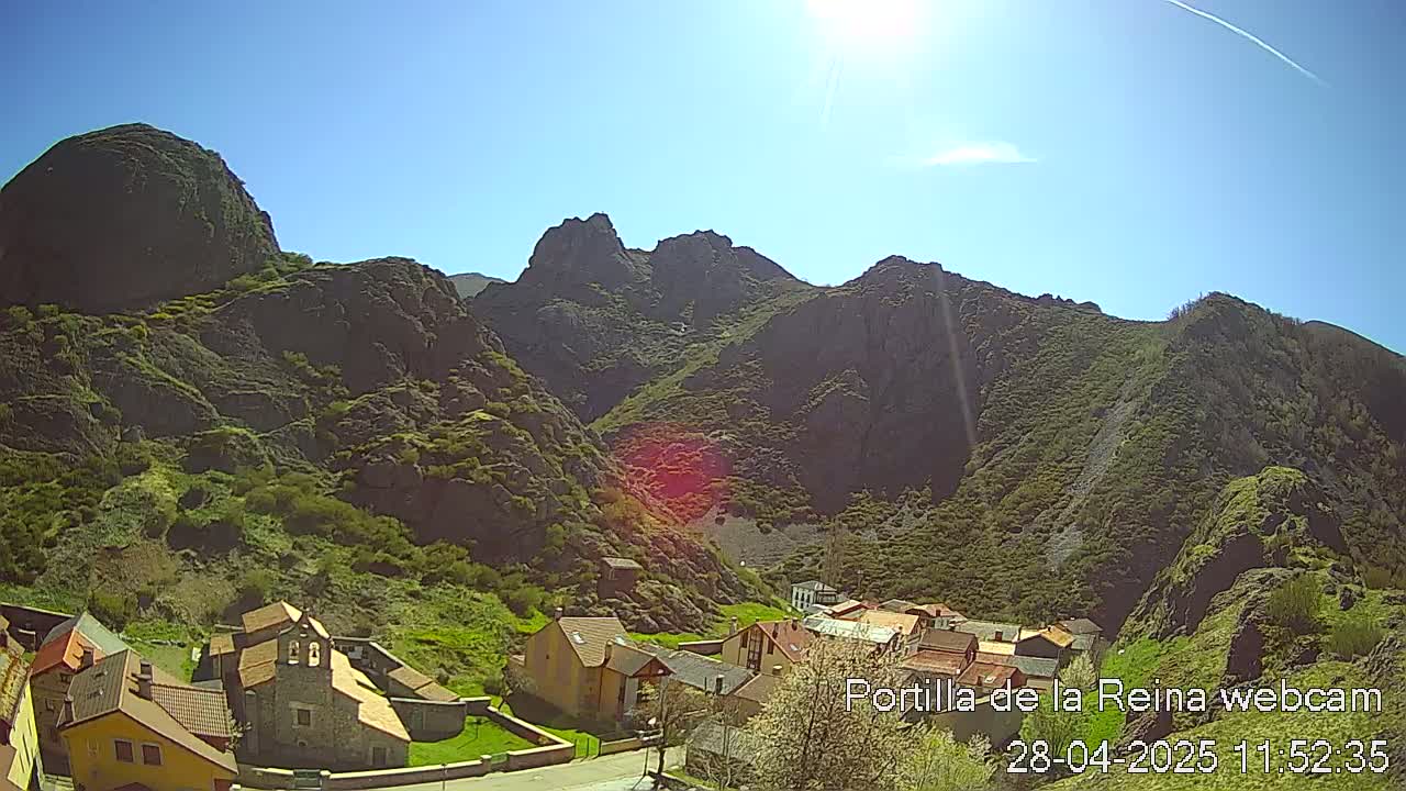 A sunny day reveals a small village nestled at the base of large, rocky mountains.