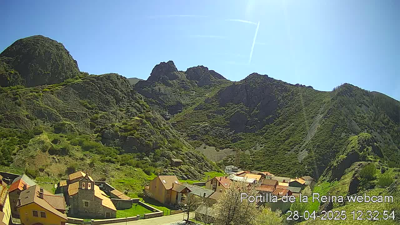 A small village nestled in a valley surrounded by rocky, green-covered mountains under a clear blue sky.