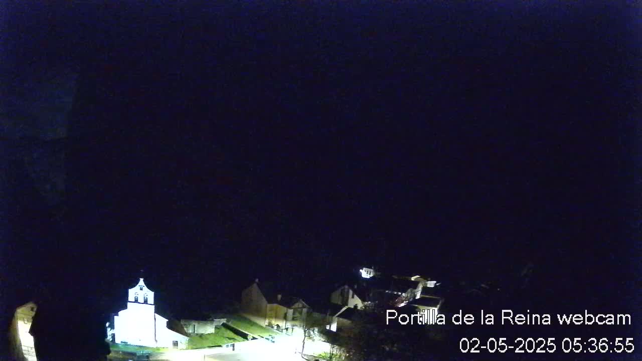 A nighttime view of a small village with a brightly lit church, under a dark, clear sky.