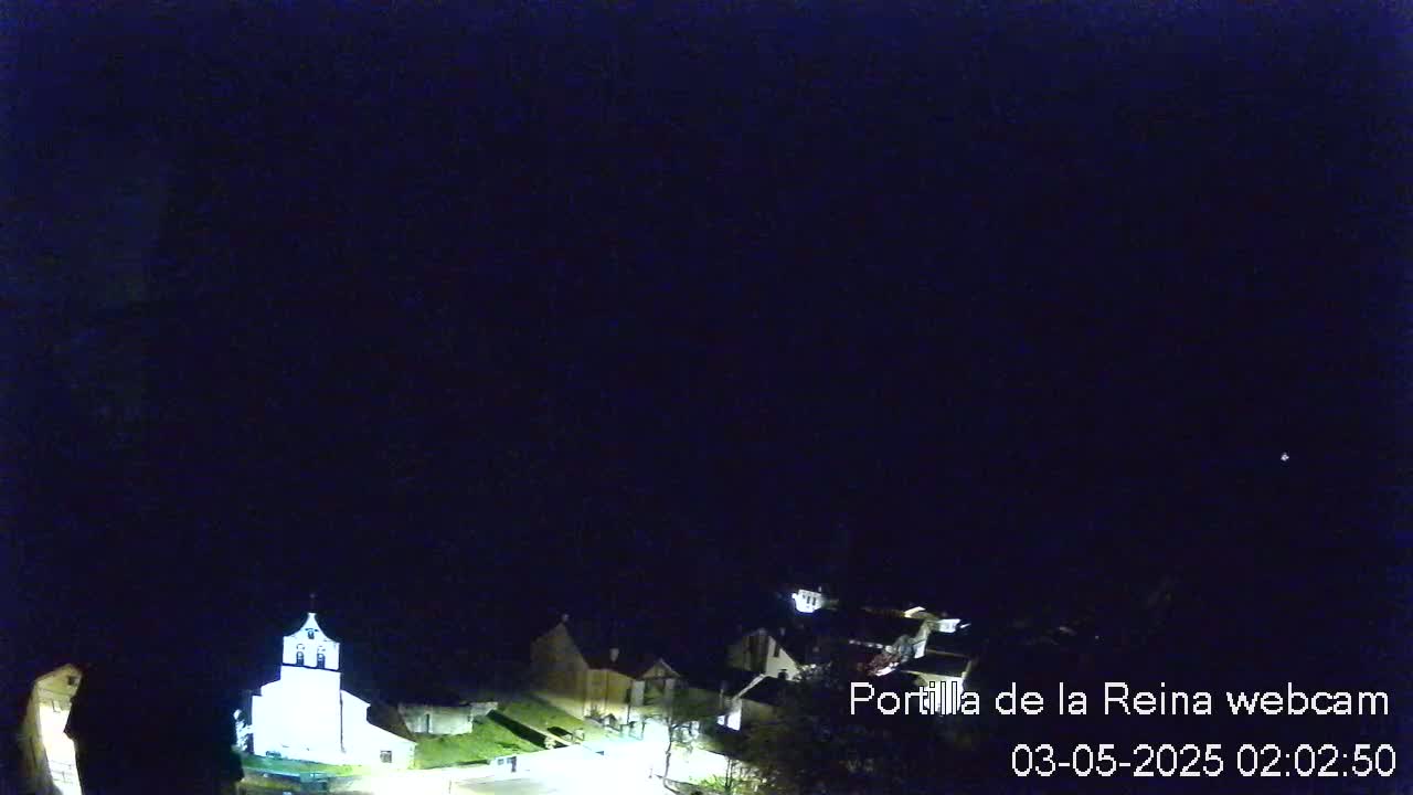 A nighttime, high-angle view shows a small village with a brightly lit church, under a dark, clear sky.