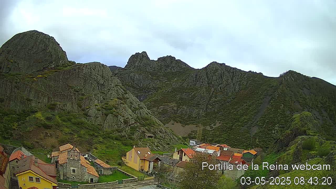 A small village nestled in a valley surrounded by steep, rocky mountains under an overcast sky.