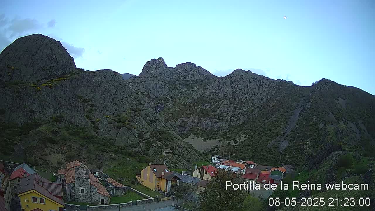 A small village nestled at the base of large, rocky mountains under a clear, twilight sky.