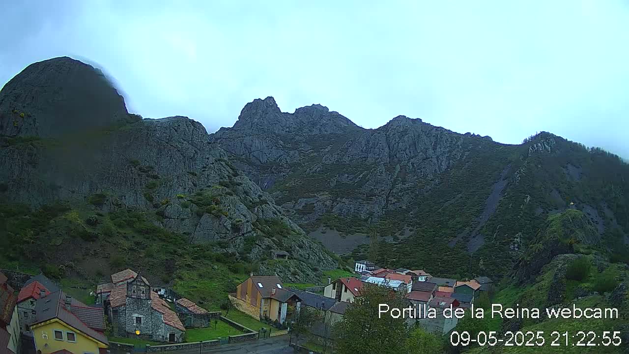 A small village nestled in a valley surrounded by steep, rocky mountains under an overcast sky.