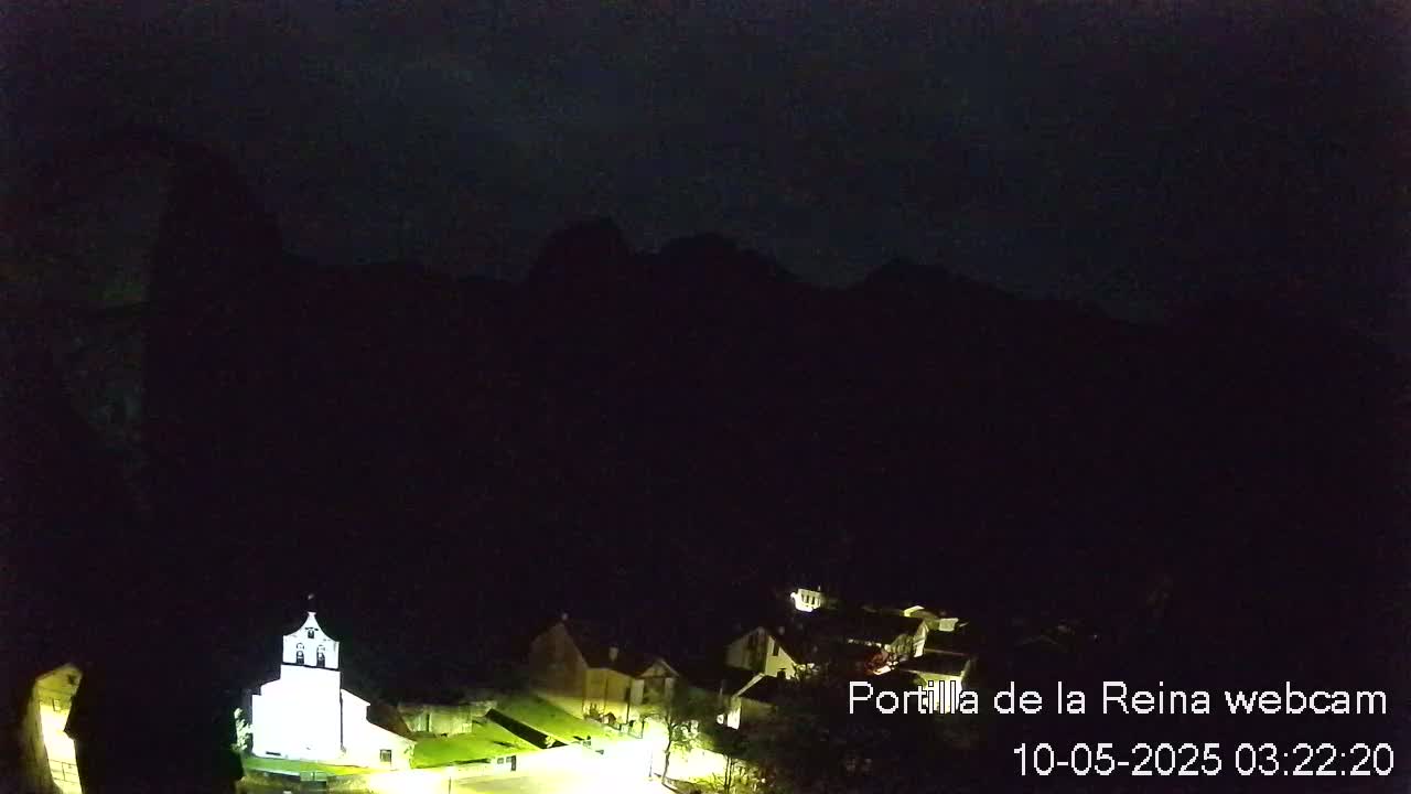 A nighttime view of a small village nestled at the base of dark mountains under a clear, dark sky.
