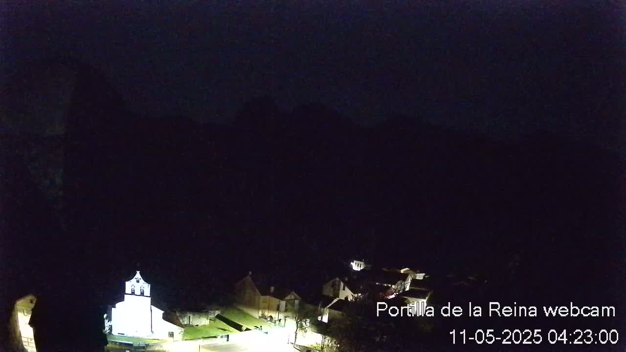 A nighttime, low-light view of a small village nestled beneath a dark mountain range.