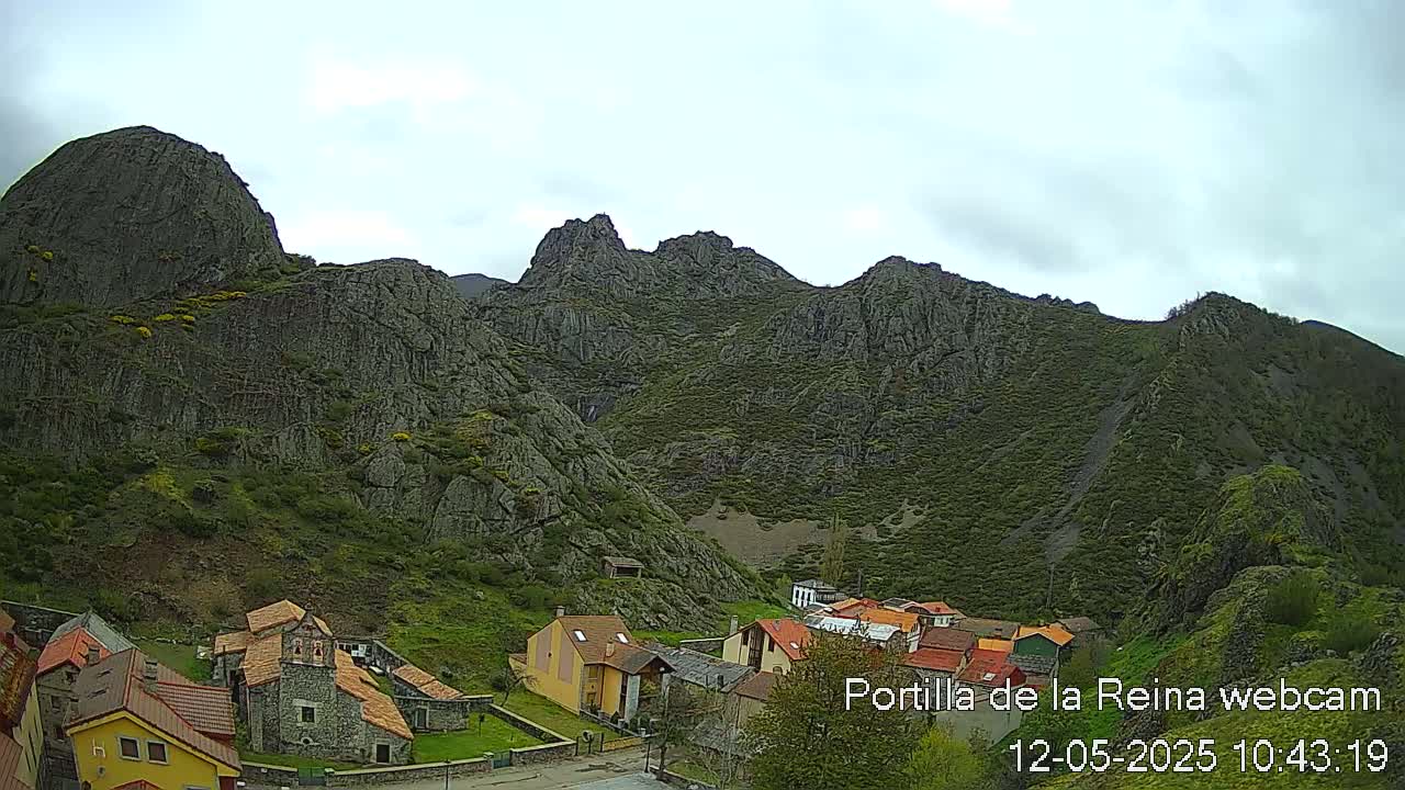 A small village nestled at the base of a large, rocky mountain range under a cloudy sky.