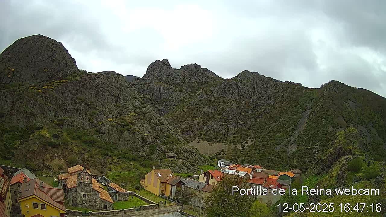 A small village nestled at the base of a rocky mountain range under an overcast sky.