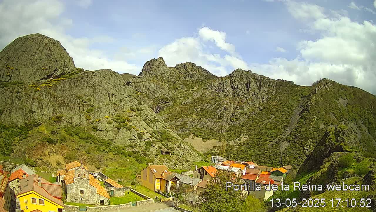 A small village nestled in a valley between rocky, green-covered mountains under a partly cloudy sky.