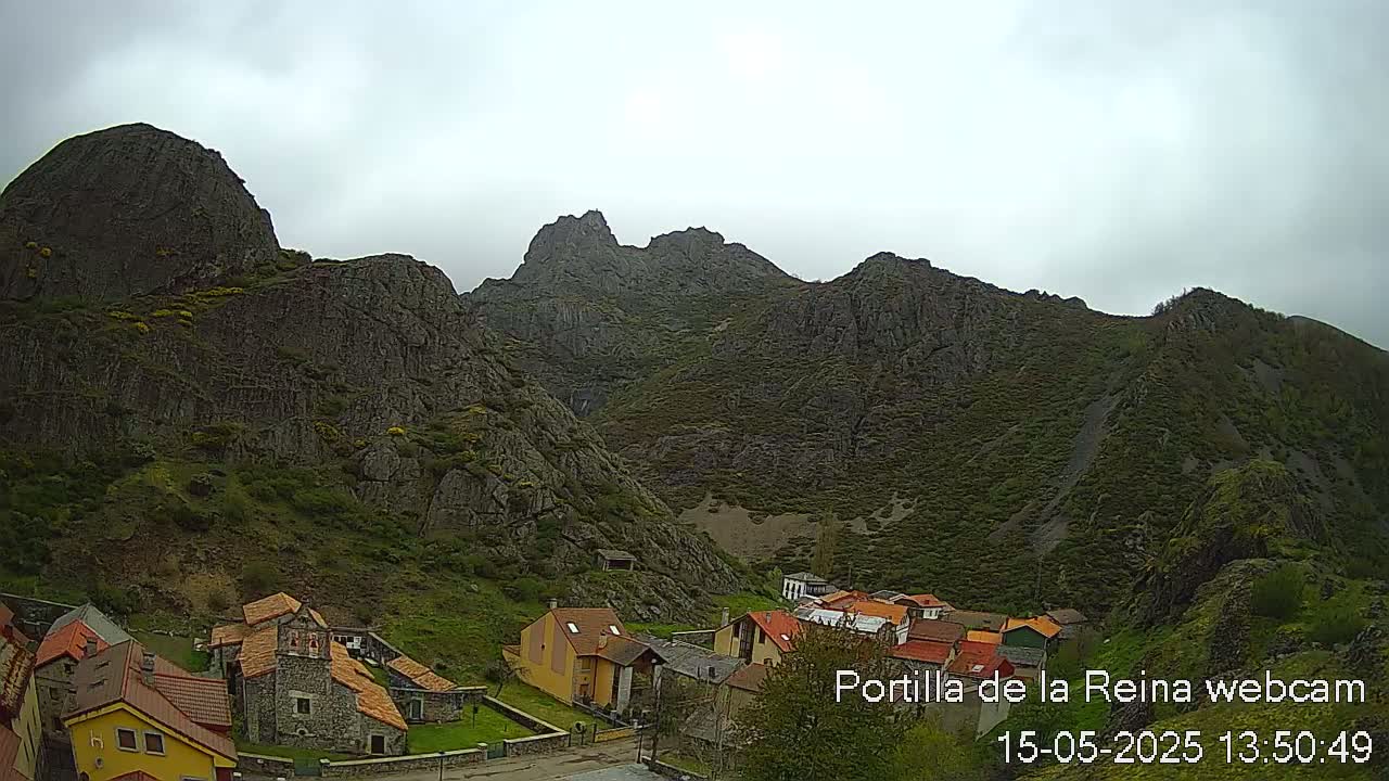 A small village nestled at the base of a rocky, mountainous landscape under an overcast sky.