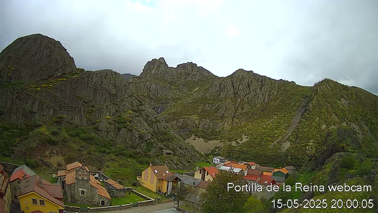 A small village nestled in a valley surrounded by rocky, green-covered mountains under an overcast sky.