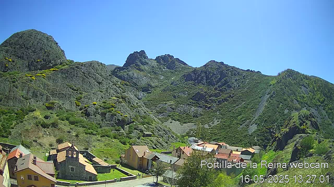 A small village nestled in a valley surrounded by rocky, green mountains under a clear blue sky.