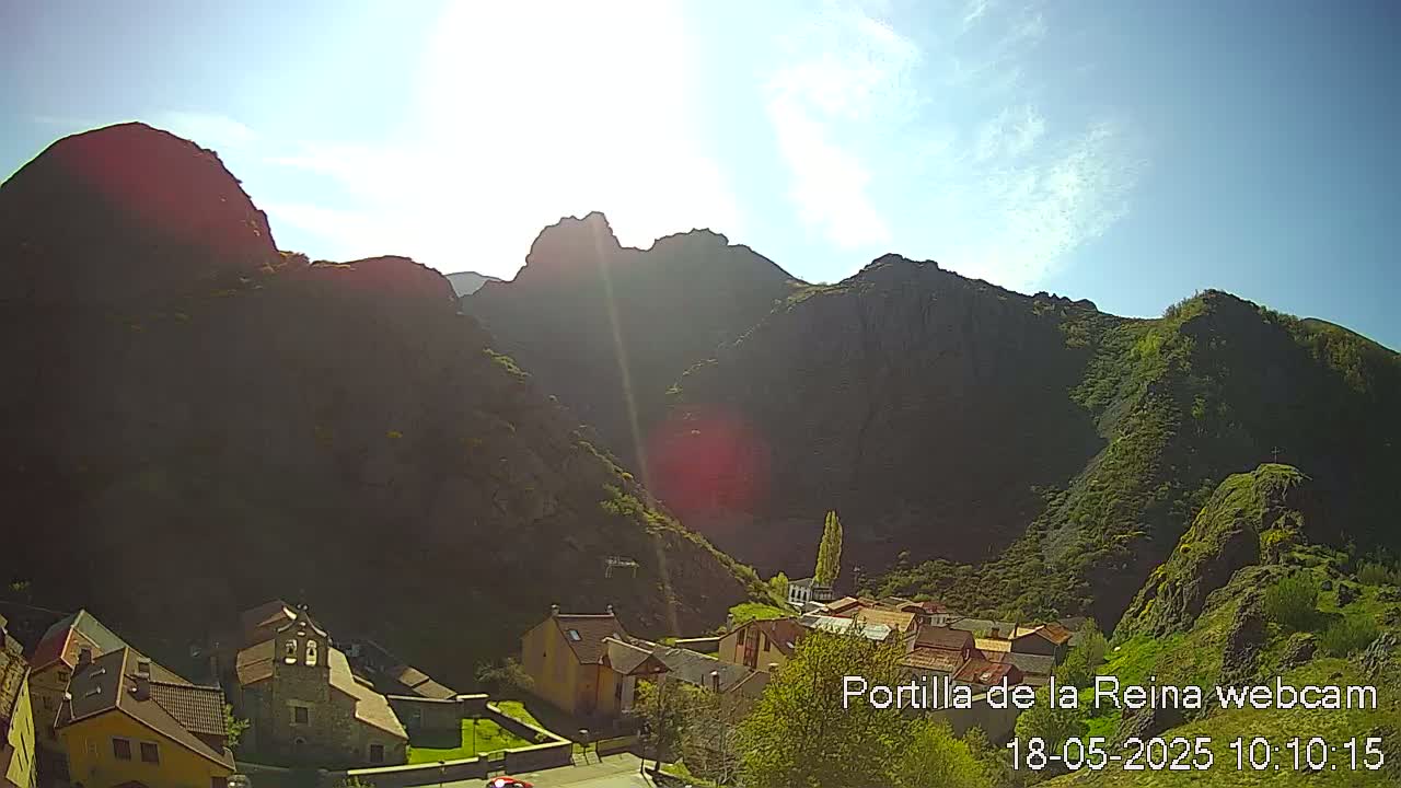 A sunny day reveals a small village nestled in a valley between large, dark mountains.