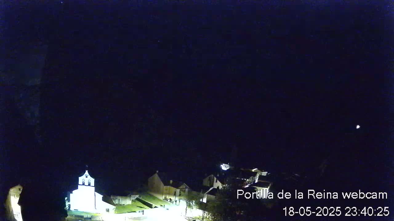 A nighttime, high-angle view of a small village with a brightly lit church, under a clear, dark sky.
