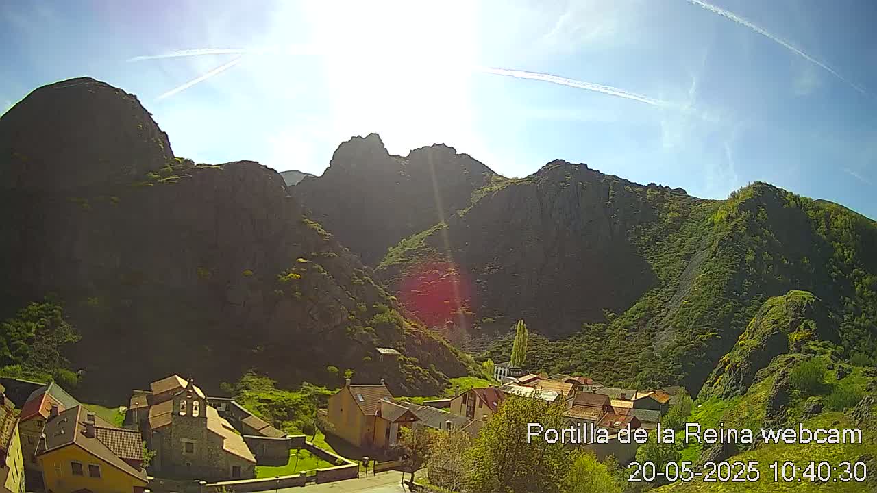A sunny day reveals a small village nestled in a valley surrounded by steep, rocky mountains.