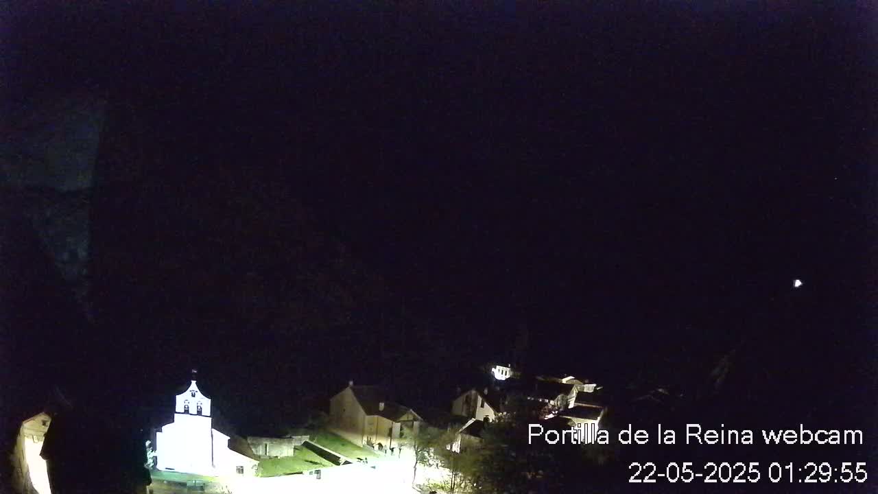 A nighttime view of a small village nestled against a dark mountain, illuminated by artificial light.