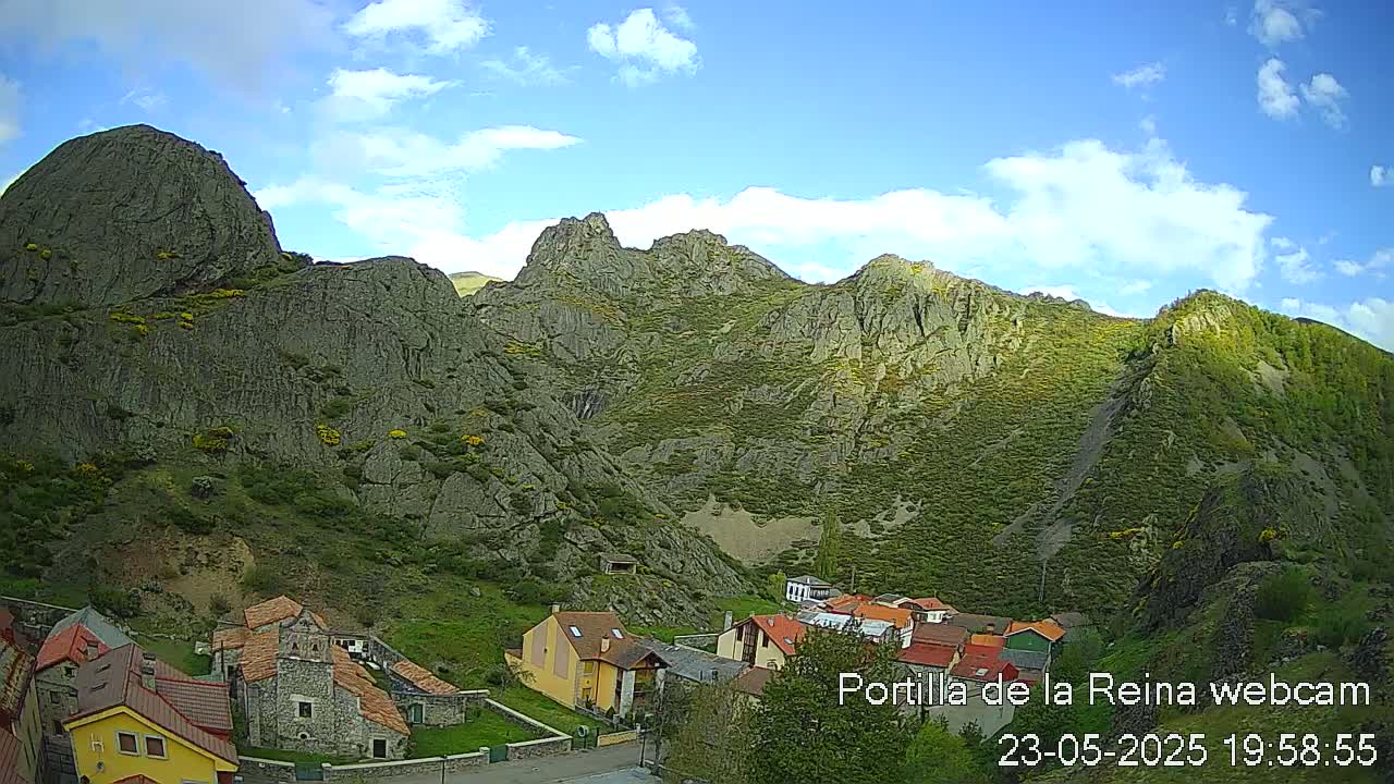 A small village nestled at the base of a large, rocky mountain under a partly cloudy sky.