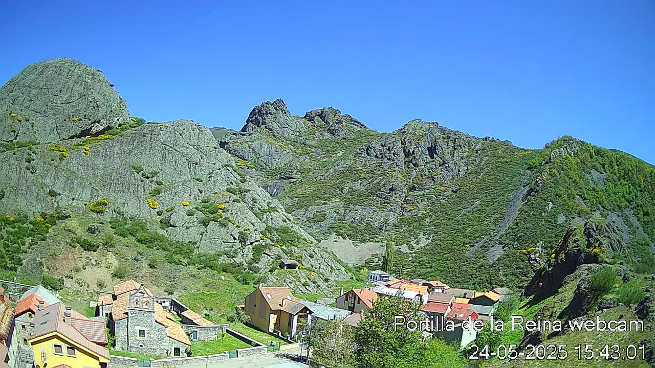 A small village nestled in a valley between rocky, green-covered mountains under a clear blue sky.