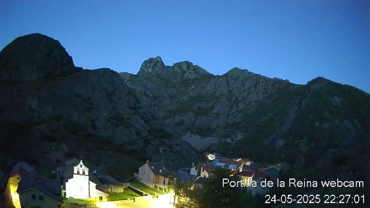 A small village nestled in a valley between dark, rocky mountains under a twilight sky.