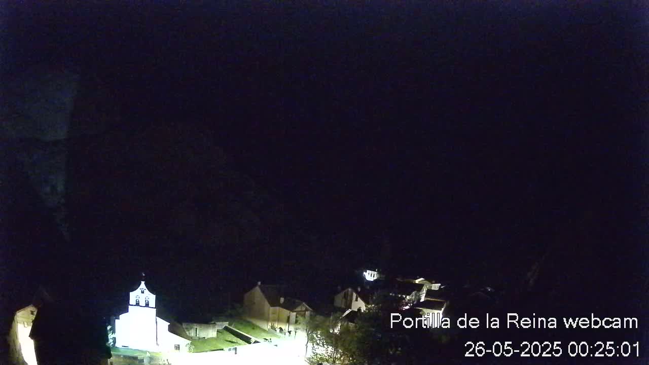 A nighttime view of a small village nestled against a dark mountainside, illuminated by artificial light.