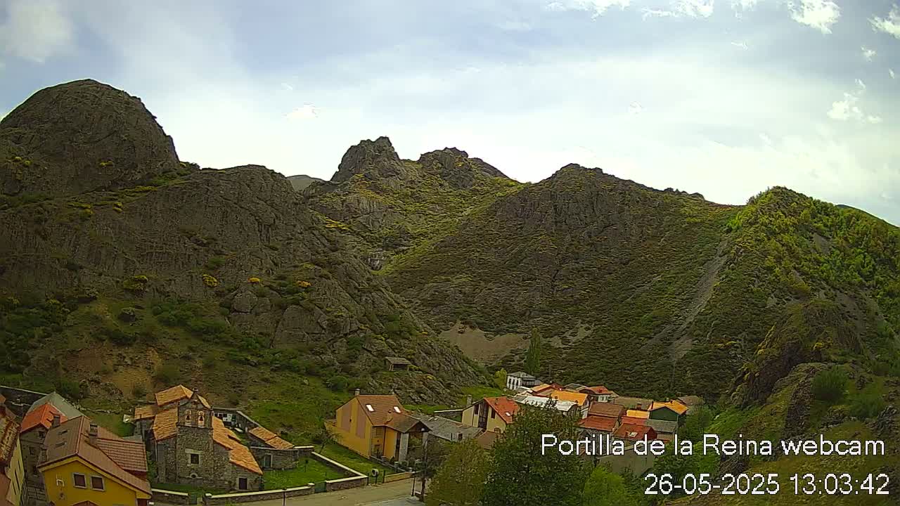 A small village nestled in a valley surrounded by rocky, mountainous terrain under a partly cloudy sky.