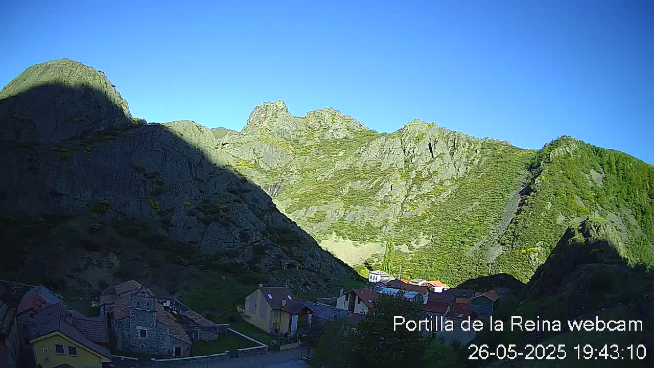 A small village nestled in a valley between rocky, green-covered mountains under a clear blue sky.