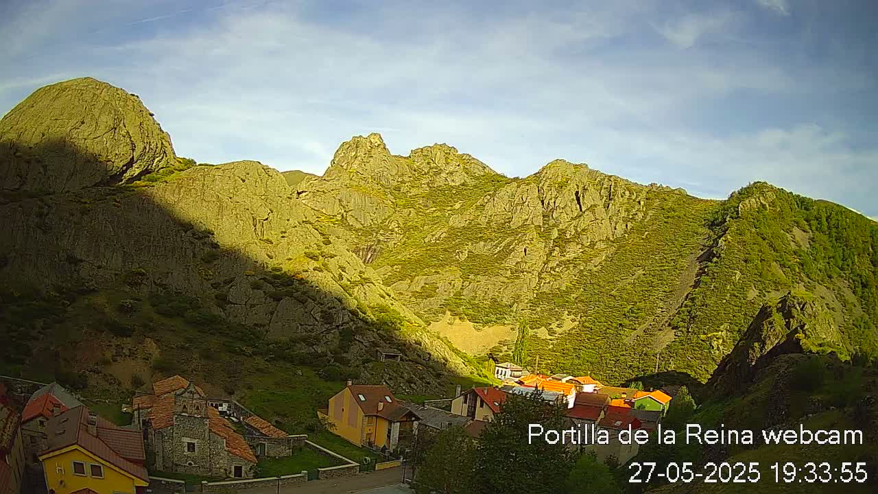 A small village nestled in a valley between large, rocky mountains, under a mostly clear sky.