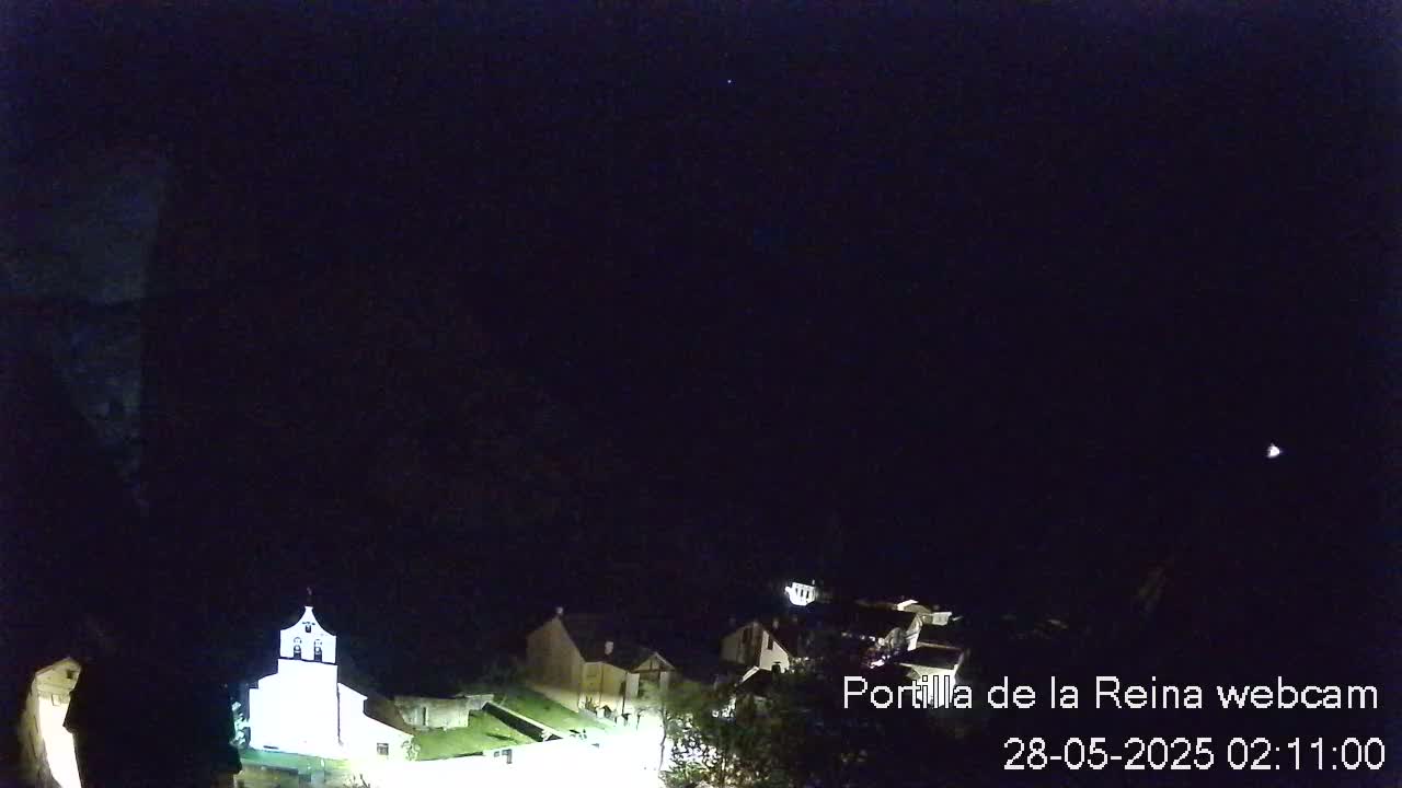 A nighttime, high-angle view of a small village with a church illuminated, under a dark, clear sky.