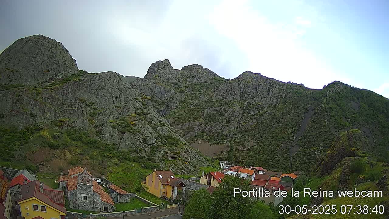 A small village nestled at the base of a large, rocky mountain under a mostly cloudy sky.