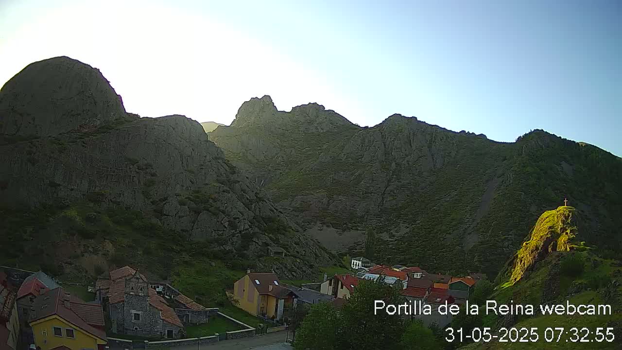 A small village nestled in a valley surrounded by rugged, rocky mountains under a clear, bright sky.