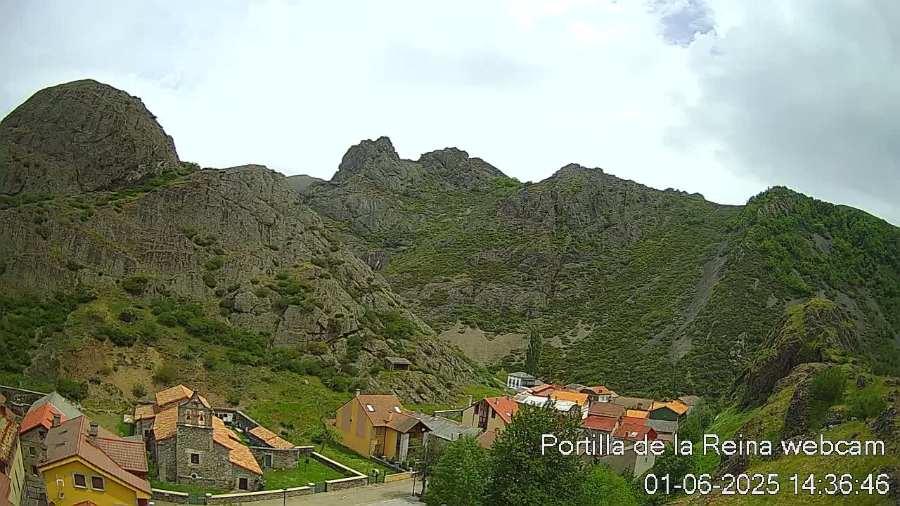 A small village nestled in a valley between steep, rocky mountains under a partly cloudy sky.