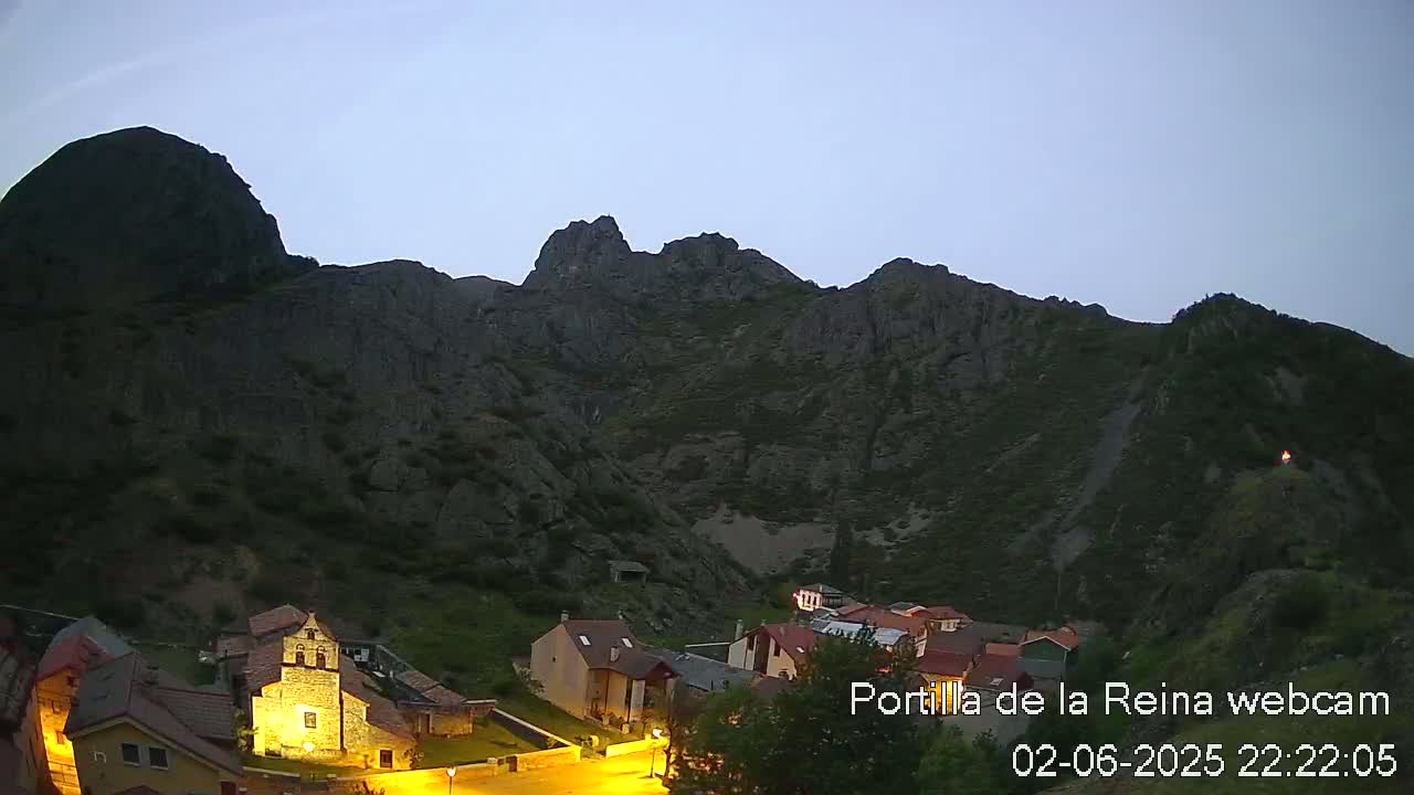 A small village nestled at the base of a large, dark mountain range under a twilight sky.