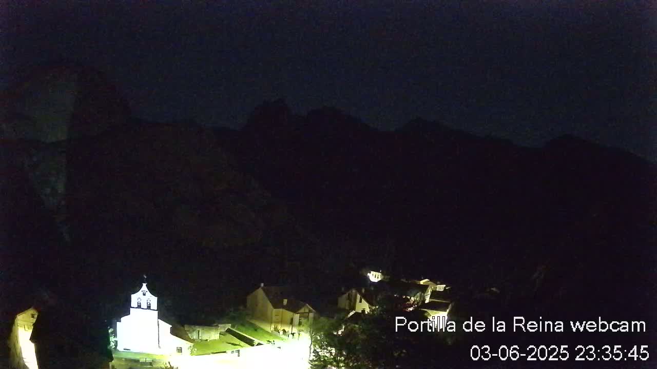 A small village nestled at the base of dark mountains at night, illuminated by a few lights.