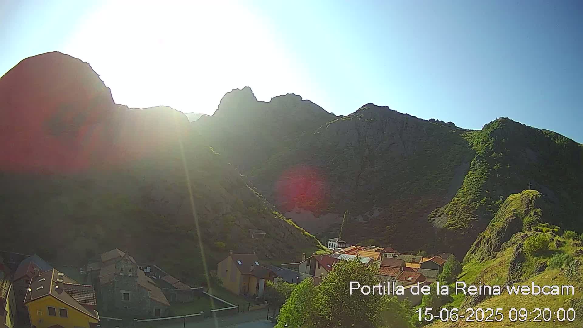 A small village nestled in a valley between sunlit, rocky mountains on a clear, sunny day.
