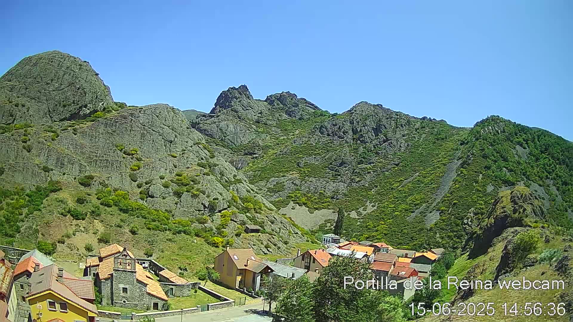 A small village nestled in a valley between rocky, green-covered mountains under a clear blue sky.