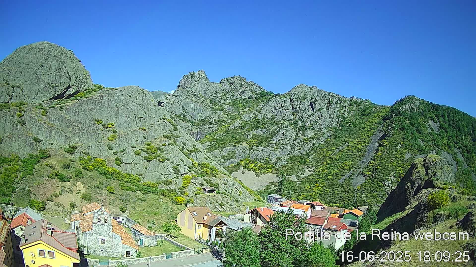 A small village nestled in a valley surrounded by steep, rocky mountains under a clear blue sky.