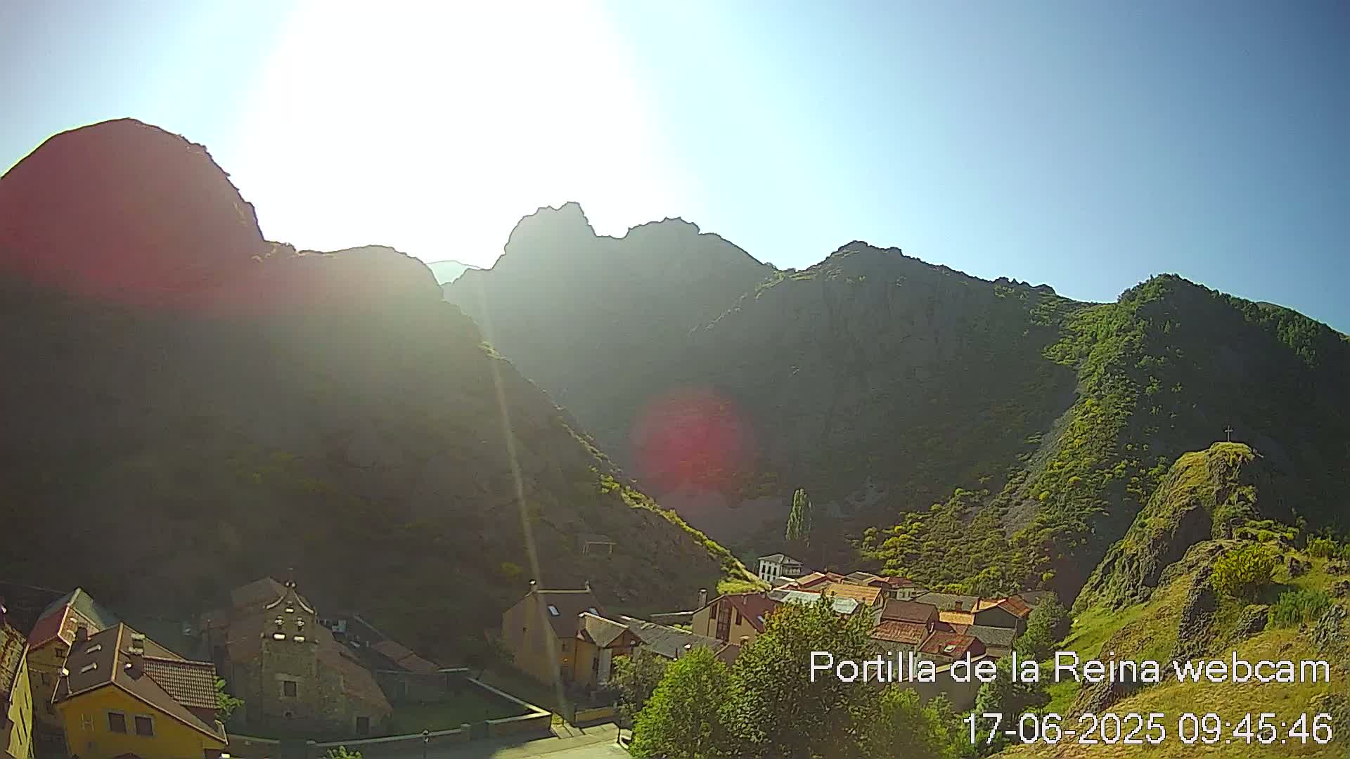 A small village nestled in a valley between sunlit, rocky mountains on a clear, sunny day.