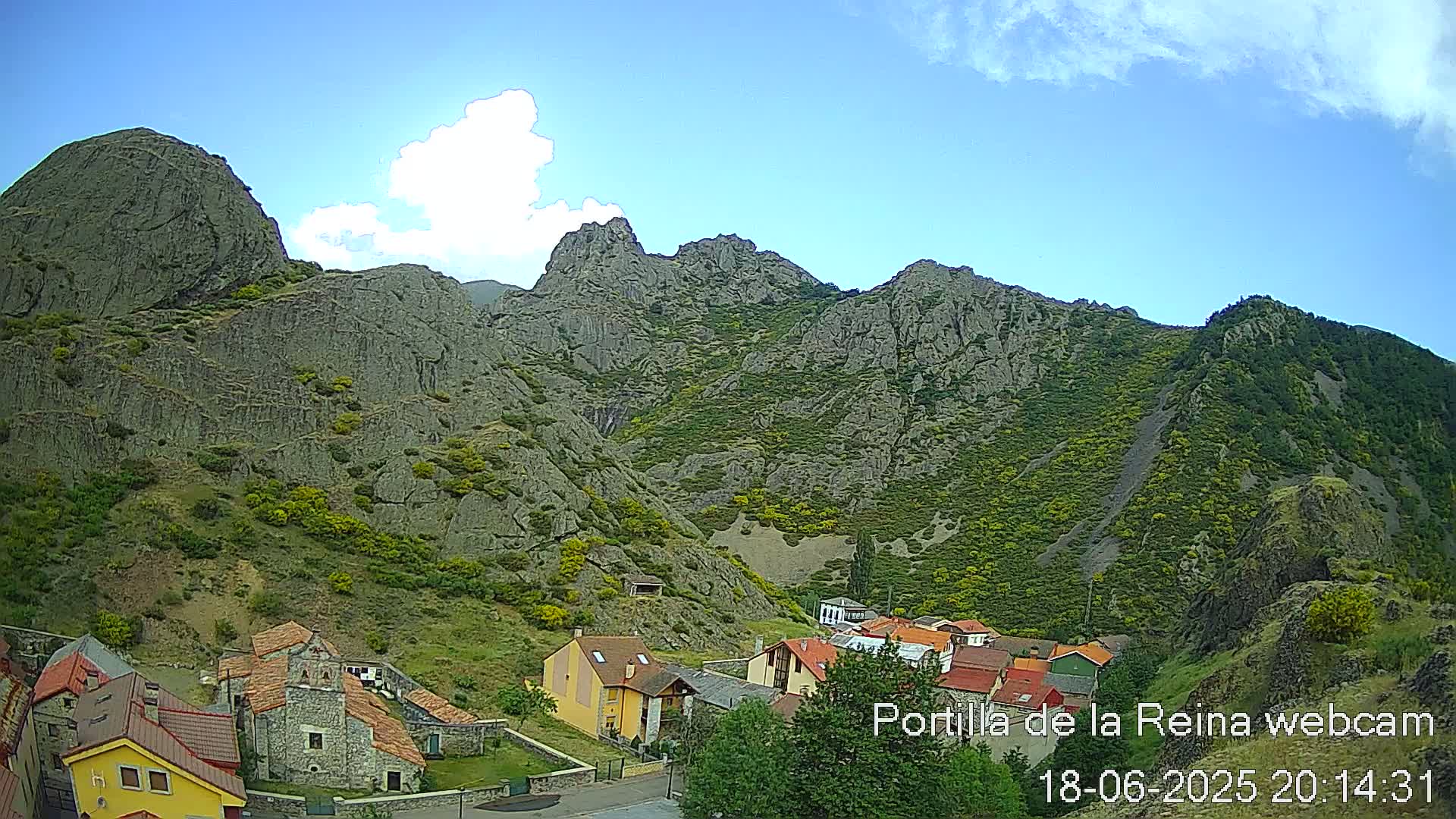 A small village nestled in a valley surrounded by steep, rocky mountains under a mostly sunny sky with a few scattered clouds.