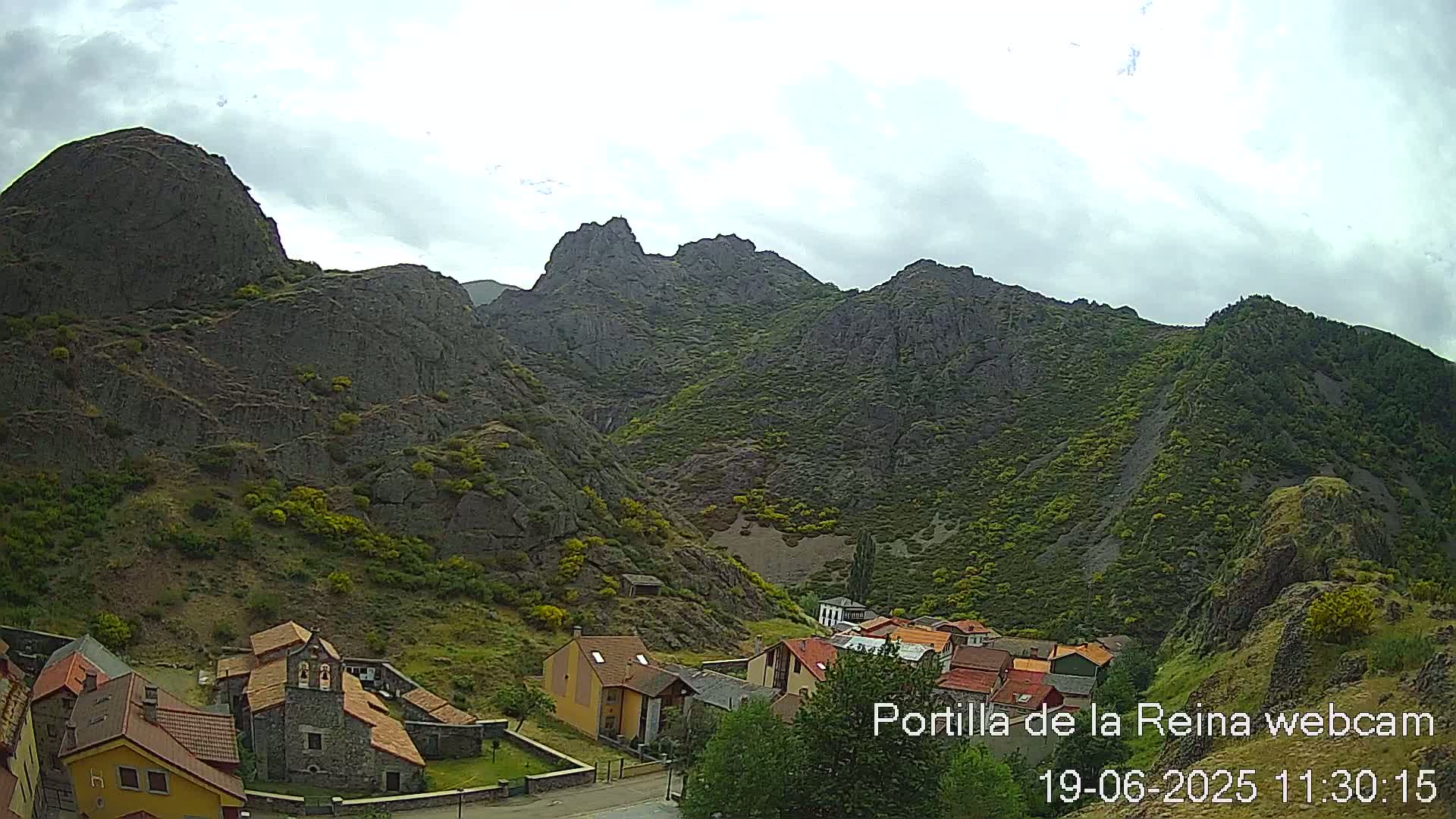 A small village nestled in a valley surrounded by rocky mountains under a cloudy sky.