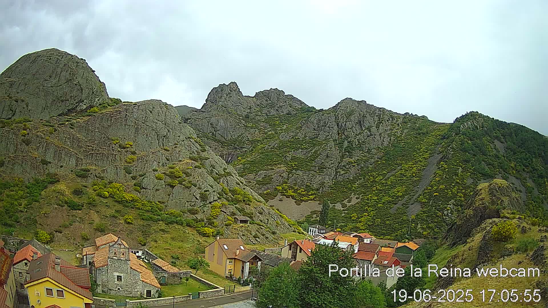 A small village nestled at the base of a rocky mountain range under an overcast sky.